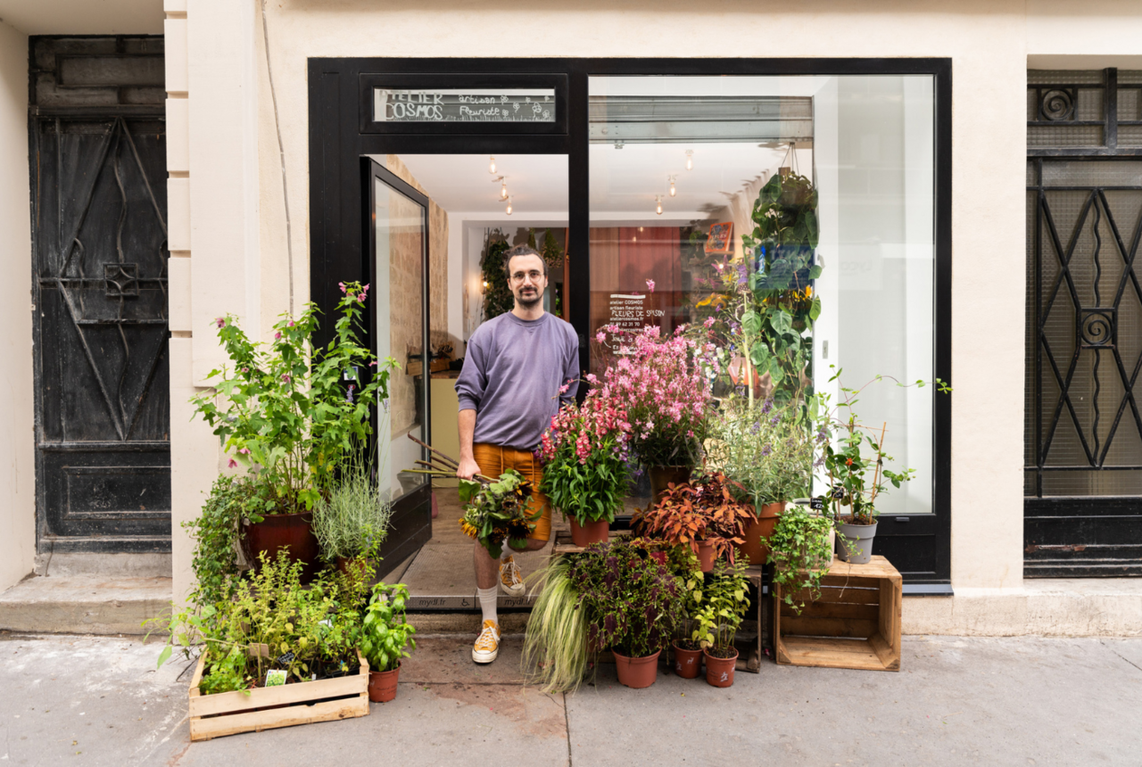 Le propriétaire d'Ateliers Cosmos à Paris 19ᵉ photographié devant la vitrine de son atelier floral.