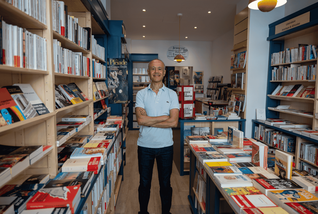 Mustapha, libraire souriant dans sa boutique L’Amie Prodigieuse, installée dans le 5ᵉ arrondissement de Paris.